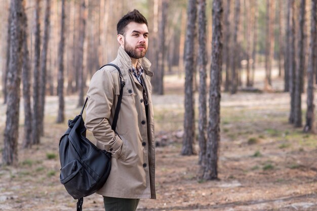 Портрет молодой мужской путешественник держит рюкзак на плече в лесу