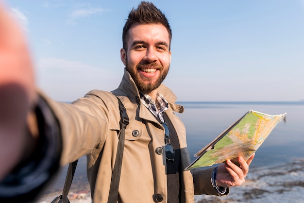 Портрет молодого мужского путешественника, держащего карту в руке, делающей селфи