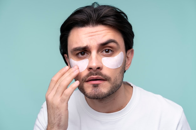 Portrait of a young man applying under-eye patches