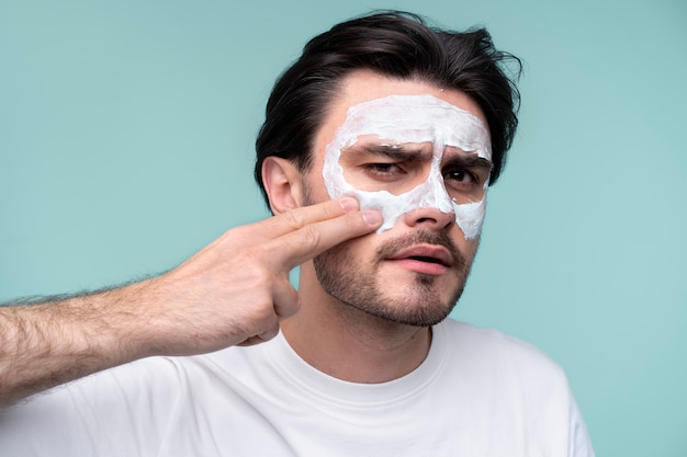 Free photo portrait of a young man applying face mask on his face