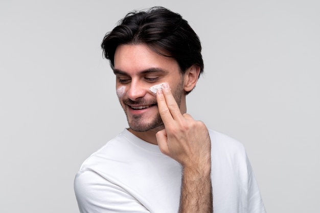 Free photo portrait of a young man applying moisturizer on his face