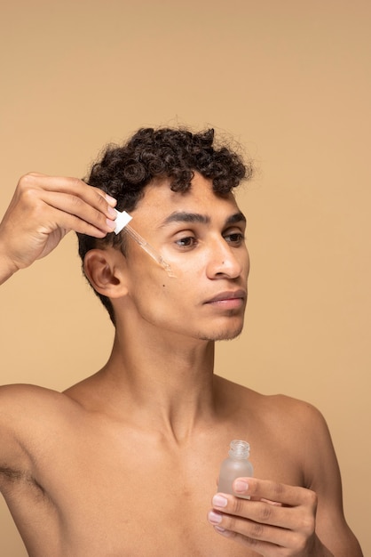 Free photo portrait of a young man applying serum on his face