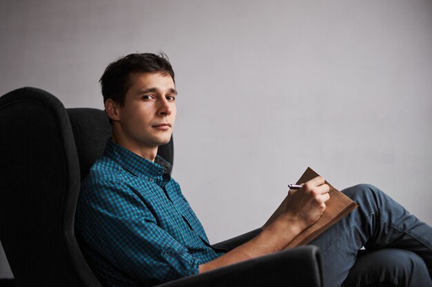 Portrait of young man in armchair in front of grey wall