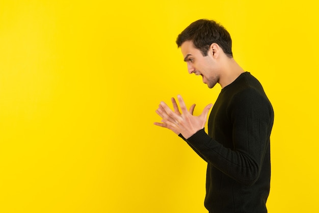 Portrait of young man in black sweatshirt screaming on yellow wall