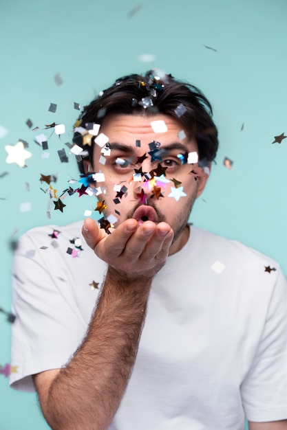 Portrait of a young man blowing confetti from his hand