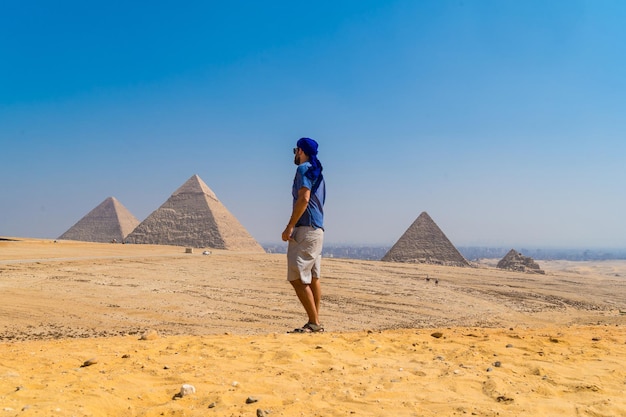 Foto gratuita ritratto di un giovane uomo con un turbante blu che cammina accanto alle piramidi di giza, il cairo, egitto