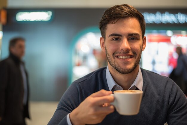 カメラのクローズアップを見て笑顔でコーヒーを飲む若い男の肖像画