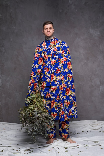 Portrait of a young man in floral clothes holding green plant twigs looking at camera