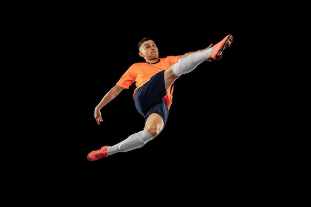 Free photo portrait of young man football playing in motion training isolated over black studio background kicking ball