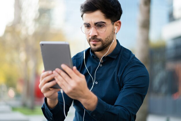 屋外に立っているときにデジタルタブレットでビデオ通話をしている若い男の肖像画