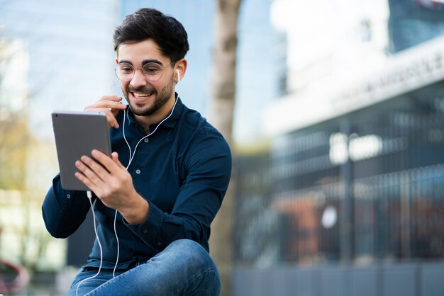 屋外に立っているときにデジタルタブレットでビデオ通話をしている若い男の肖像画