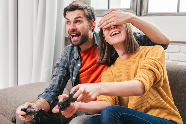 Free photo portrait of a young man hiding his wife's eyes while playing the video game