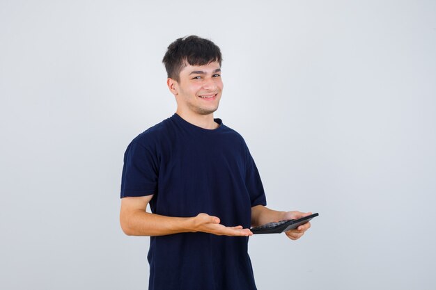 Portrait of young man holding calculator in black t-shirt and looking cheerful front view