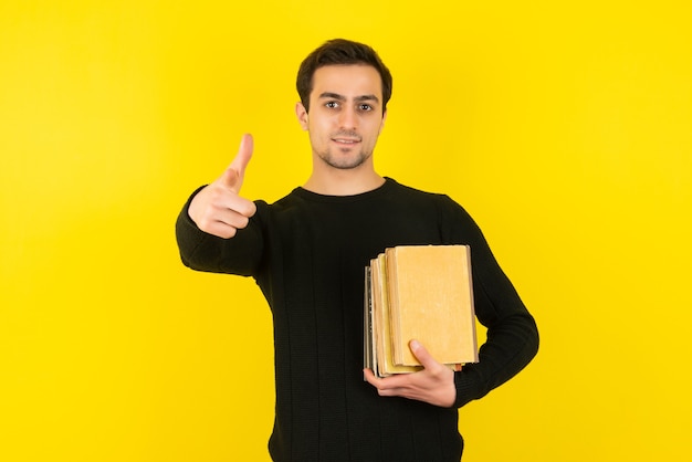 Portrait of young man holding college books on yellow wall