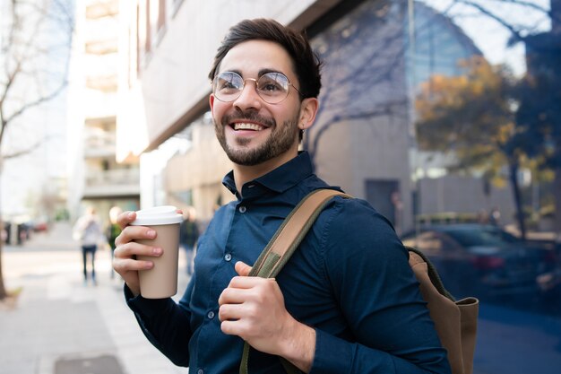 거리에서 야외에서 걷는 동안 커피 한 잔을 들고 젊은 남자의 초상화. 도시 및 라이프 스타일 개념.