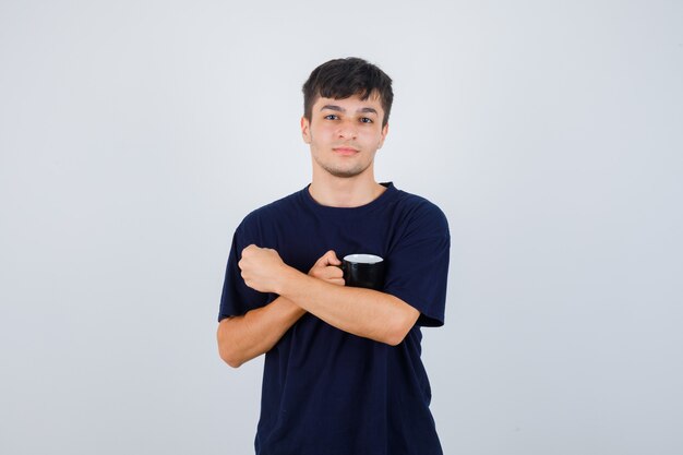 Портрет молодого человека, держащего чашку чая в черной футболке и уверенно выглядящего, вид спереди
