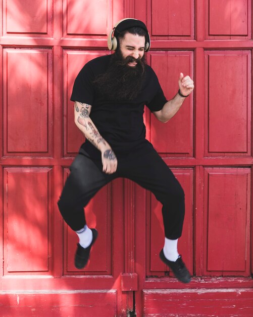 Портрет молодого человека, прыжки в воздух с наушниками на ухе против красной двери