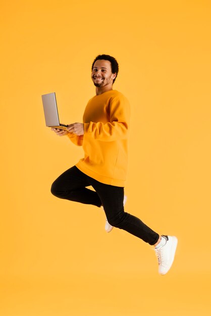 Portrait young man jumping with laptop