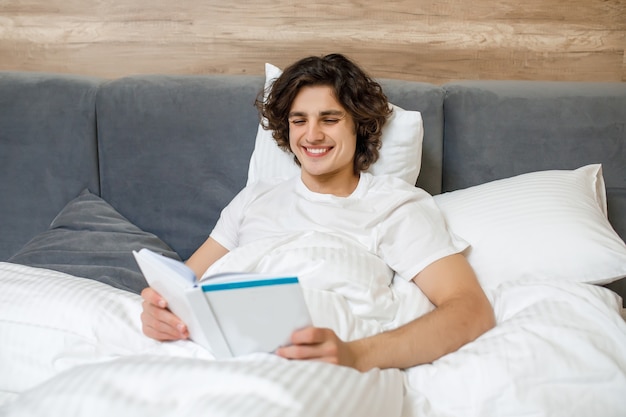 彼の寝室で週末に休んで本を読んでいる間彼のベッドに横たわっている若い男の肖像画