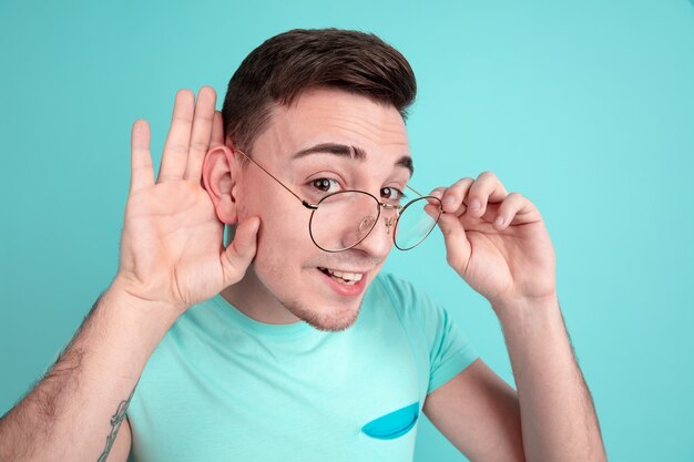 Portrait of young man listens to secrets isolated on aquamarine studio wall