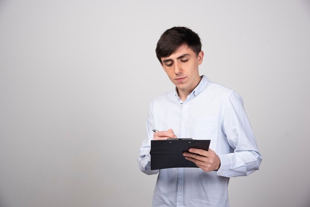 Portrait of young man looking at clipboard on gray wall.