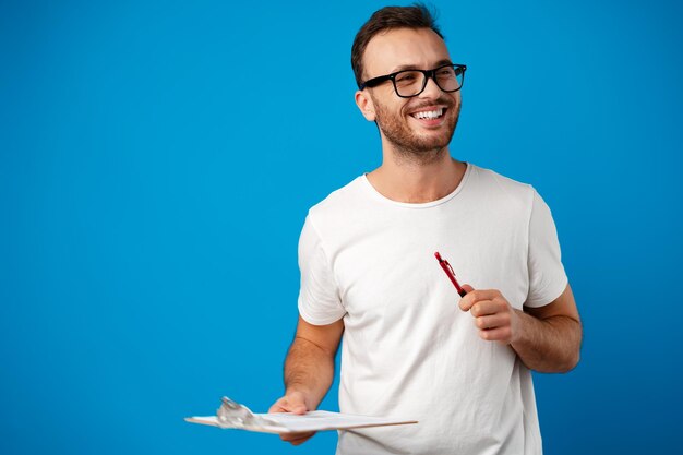 Portrait of young man making notes on clipboard against blue background