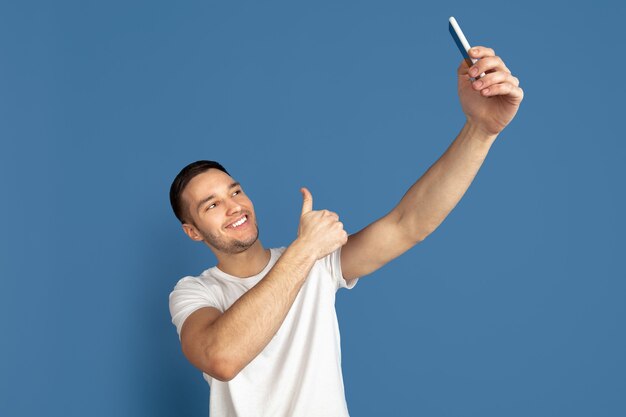 Portrait of young man making selfie photo isolated on blue studio wall