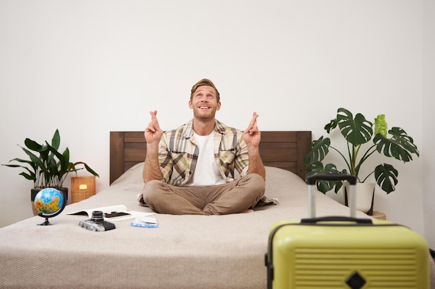 Free photo portrait of young man meditating on a bed after packing suitcase for summer holiday sitting with