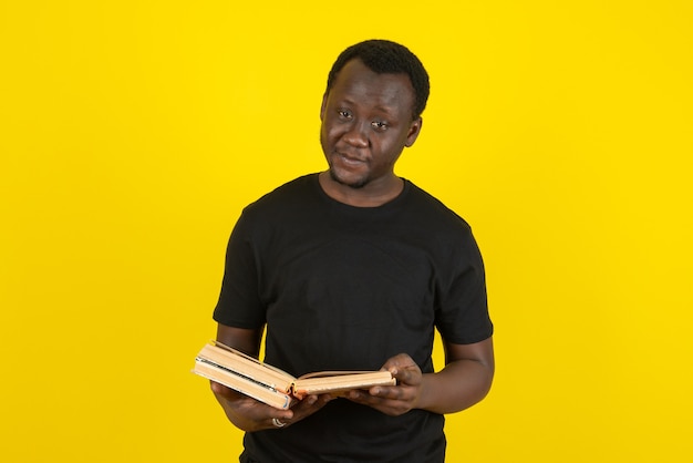 Портрет модели молодого человека, держащего книги у желтой стены