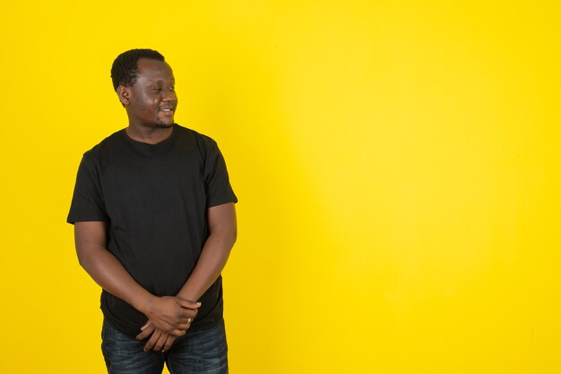 Portrait of a young man model standing and looking aside against yellow wall 