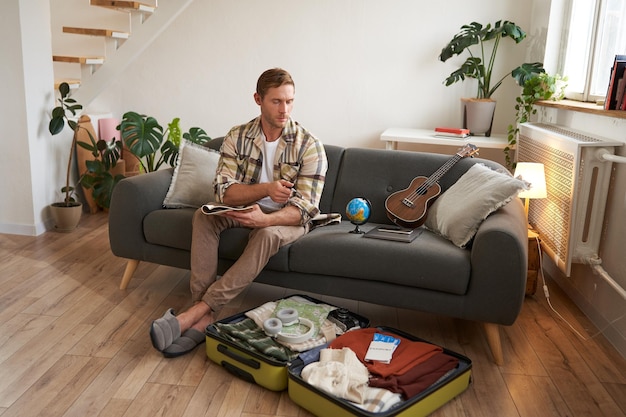 Free photo portrait of young man packing for a trip going on vacation putting clothes inside suitcase preparing