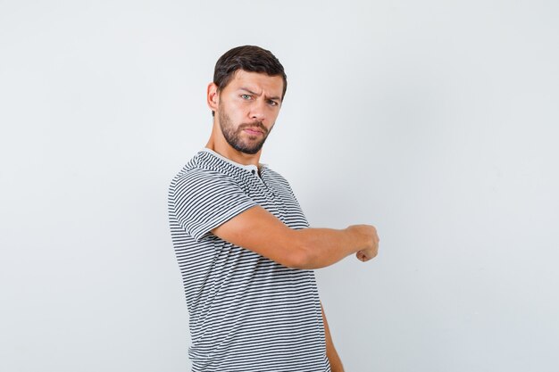 Portrait of young man pointing back in t-shirt and looking hesitative front view