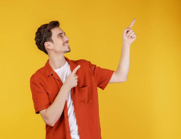 黄色のスタジオの背景に分離されたコピースペースで指を指す若い男の肖像画