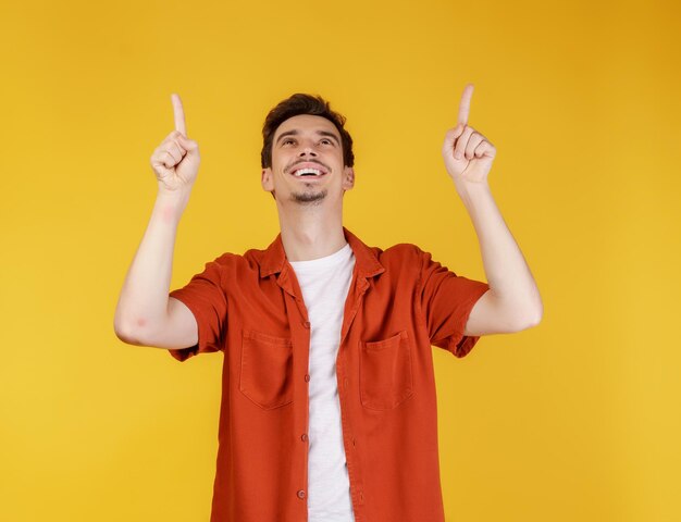 Portrait of young man pointing fingers at copy space isolated on yellow studio background