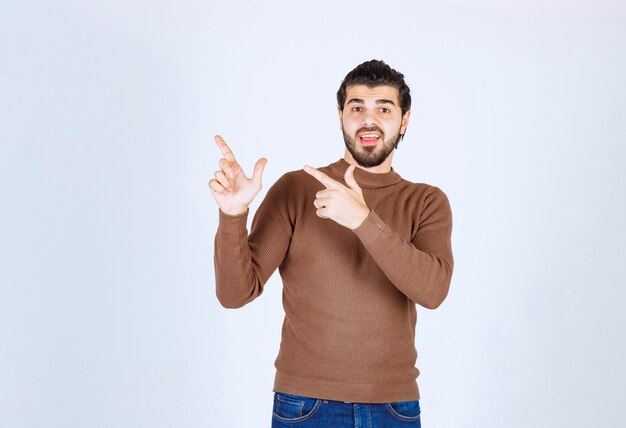 Portrait of a young man pointing fingers up at copy space isolated over white background. High quality photo