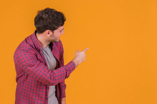 Portrait of a young man pointing his finger and looking at orange backdrop