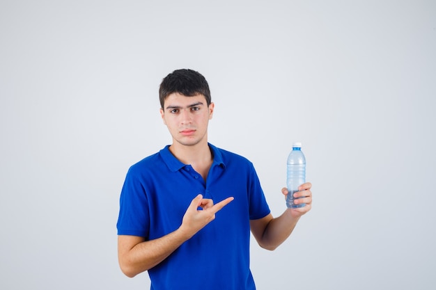 Портрет молодого человека, указывающего на пластиковую бутылку в футболке и уверенно выглядящего, вид спереди
