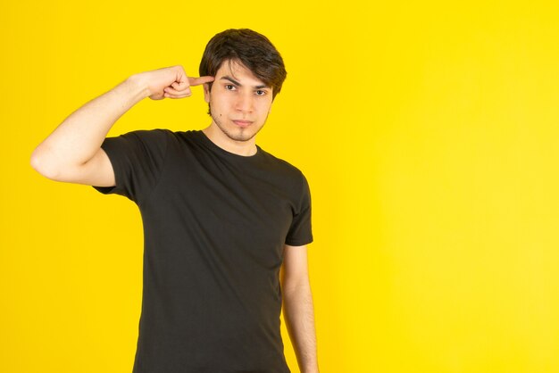 Portrait of a young man pointing at temple against yellow.