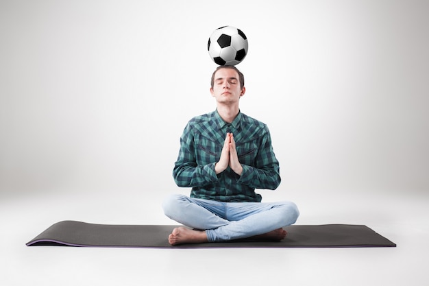 Портрет молодого человека, практикующего йогу с футбольным мячом