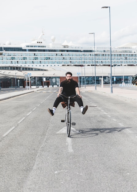 Portrait of young man riding bicycle on road with legs kicked out in front of cruise