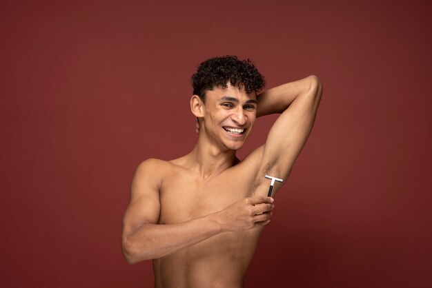 Portrait of a young man shaving his armpit with a razor