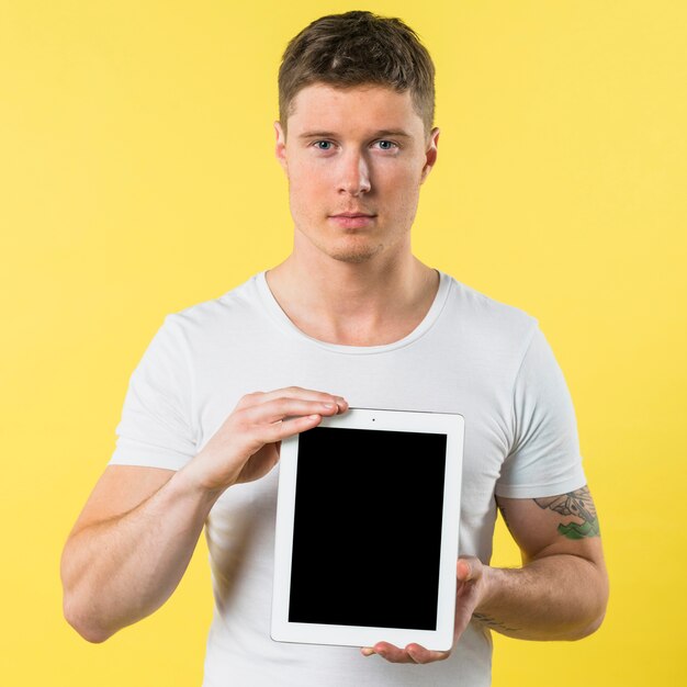 Portrait of a young man showing blank screen digital tablet against yellow backdrop