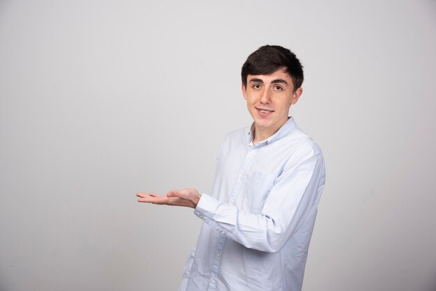 Portrait of young man showing copy space on his palm on grey wall.