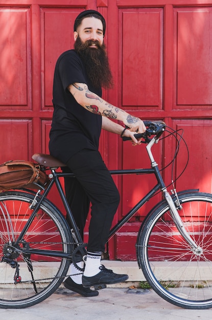 Portrait of a young man sitting on the bicycle against red door