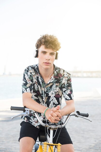 Portrait of a young man sitting on bicycle listening to music on headphone