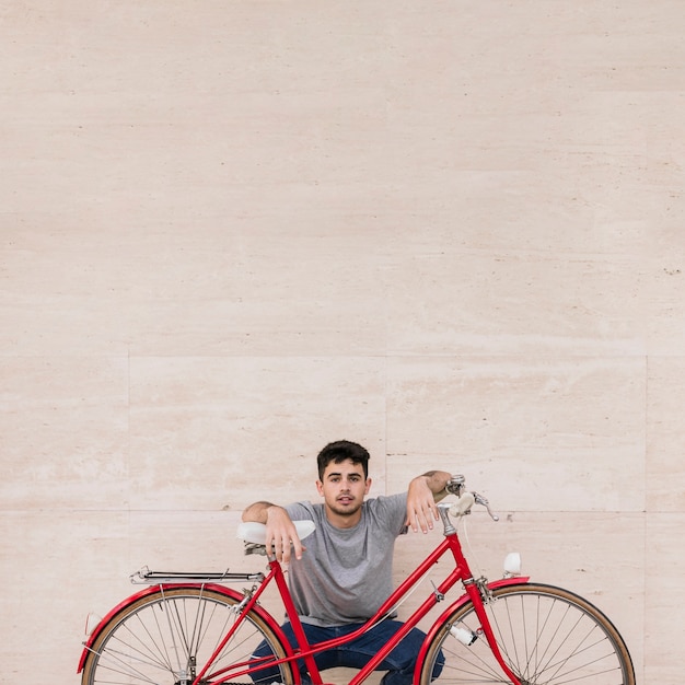 Free photo portrait of a young man sitting behind bicycle