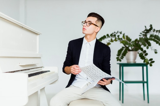 Foto gratuita ritratto di un giovane che si siede vicino allo strato musicale della tenuta del piano che distoglie lo sguardo