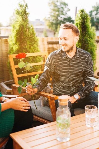 Portrait of young man sitting in restaurant giving red rose to her girlfriend