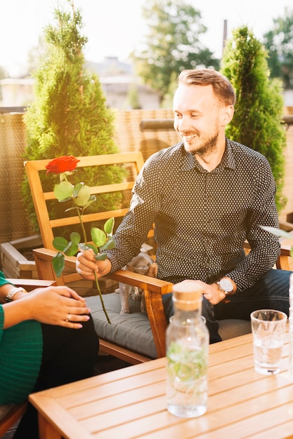 Портрет молодого человека, сидящего в ресторане, давая красной розы ее подруге