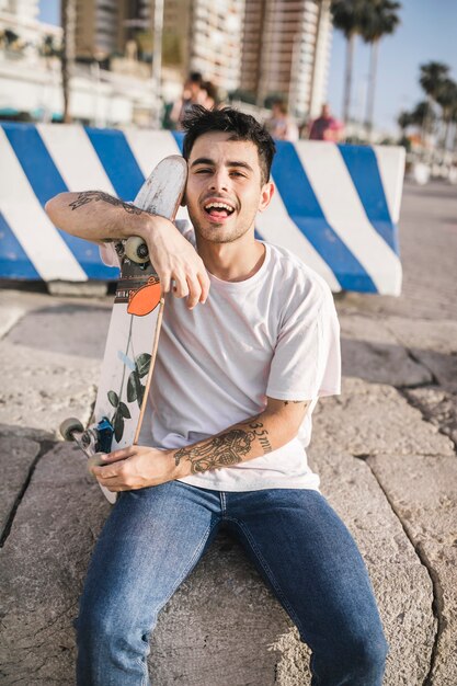 Portrait of a young man sitting on retaining wall with skateboard